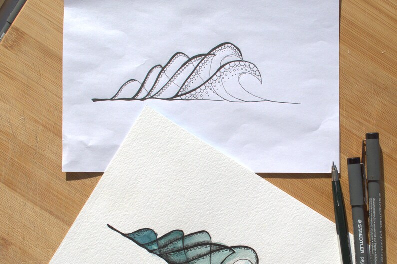 May include: A black ink line drawing of ocean waves on white paper featuring intricate circular patterns and stippling details, accompanied by a partially visible watercolor painting of waves in shades of teal and blue with three black pens.
