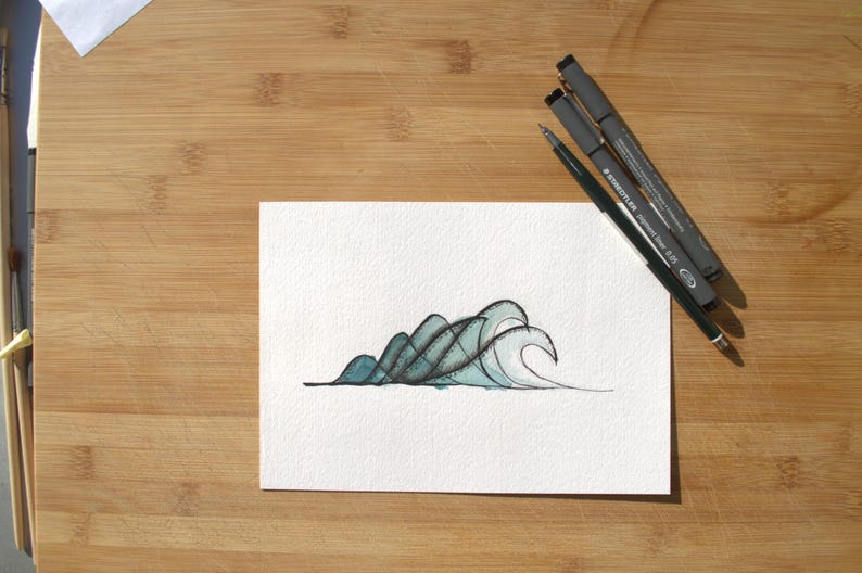 May include: A white rectangular piece of paper featuring a hand-drawn illustration of stylized ocean waves in shades of teal and black ink. Three black pens are positioned diagonally across the top right corner of the paper.