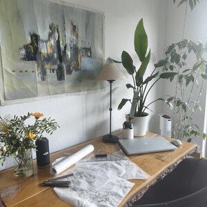 May include: A live-edge wooden desk featuring a silver laptop, a black lamp, a white vase with yellow flowers, a white cylindrical container with pens, a rolled white paper, a clear plastic triangle ruler, and sketches on white paper.