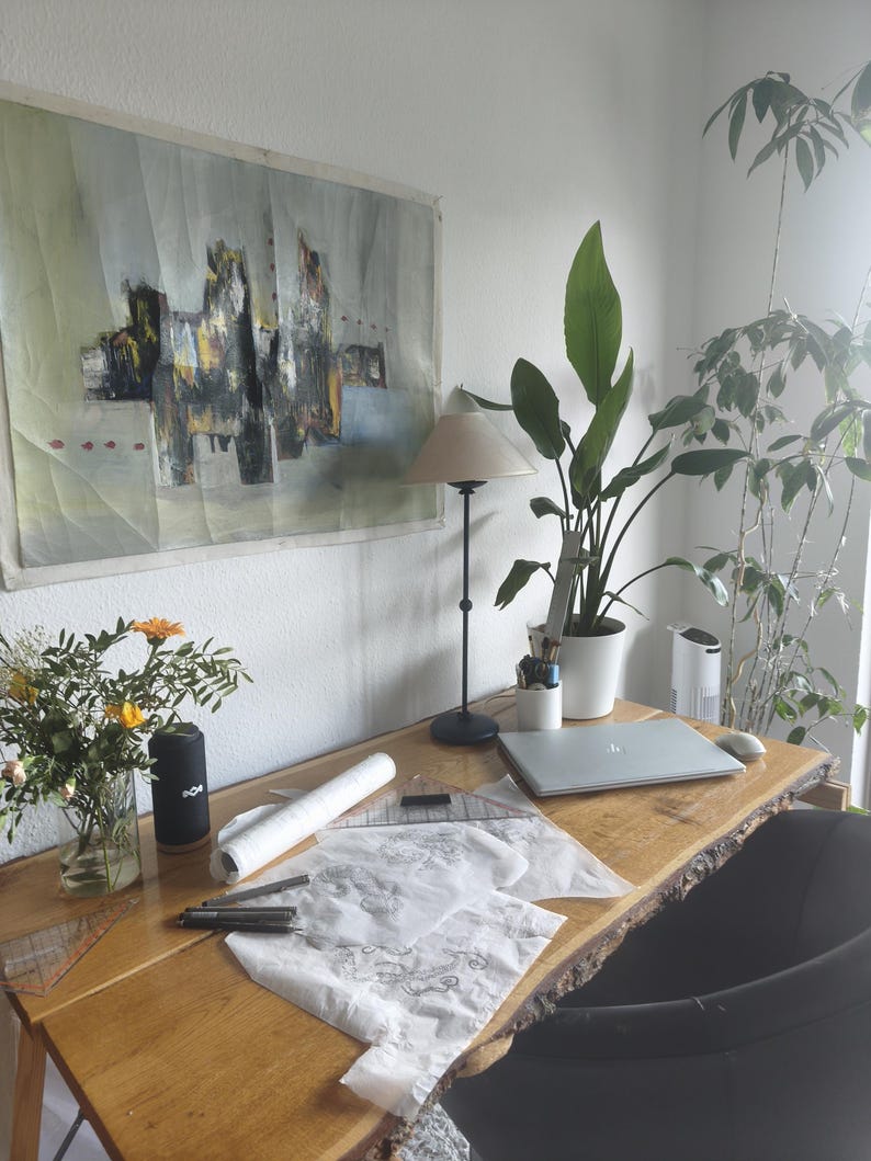 May include: A live-edge wooden desk featuring a silver laptop, a black lamp, a white vase with yellow flowers, a white cylindrical container with pens, a rolled white paper, a clear plastic triangle ruler, and sketches on white paper.
