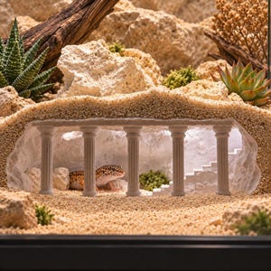 May include: A beige, textured reptile hide shaped like a classical ruin with five vertical columns and a small staircase inside. A spotted leopard gecko is resting on the sandy floor between the columns, surrounded by rocks and succulents.