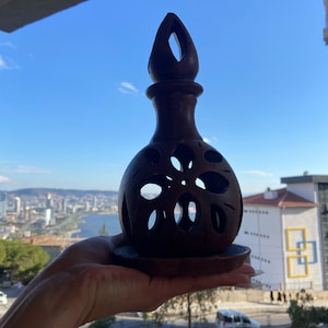Può includere: Un portacandele sferico in legno marrone scuro caratterizzato da intricati intagli floreali realizzati a mano e un collo stretto e appuntito. L'oggetto poggia su una base circolare in legno, con una finitura liscia e lucida ben visibile.