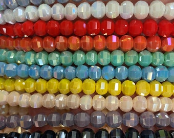 May include: Assortment of faceted glass beads in various colors, including white, red, orange, green, blue, yellow, gray, and black. The beads are arranged in rows, showcasing their iridescent shine.