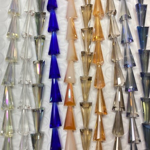 May include: Assortment of faceted glass beads in various colors, including clear, blue, brown, and beige. The beads are shaped like a triangle with a pointed tip.