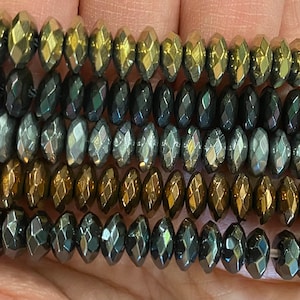 May include: A close-up of a strand of faceted glass beads in various shades of gold, silver, and black. The beads are oval-shaped and have a metallic sheen.