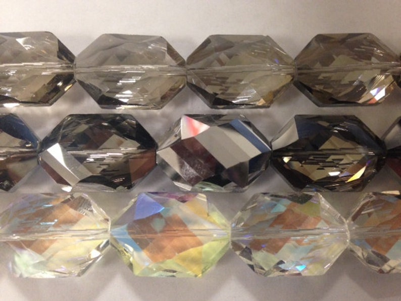 Peut inclure: Trois rang&eacute;es de perles en verre facett&eacute;es. La rang&eacute;e du haut est transparente avec une teinte fum&eacute;e. La rang&eacute;e du milieu est gris fonc&eacute; avec une finition miroir. La rang&eacute;e du bas est transparente avec une finition iris&eacute;e.