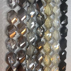 Peut inclure: Un brin de perles de verre facett&eacute;es dans diff&eacute;rentes nuances de gris, noir et transparent. Les perles sont hexagonales et ont une finition polie.