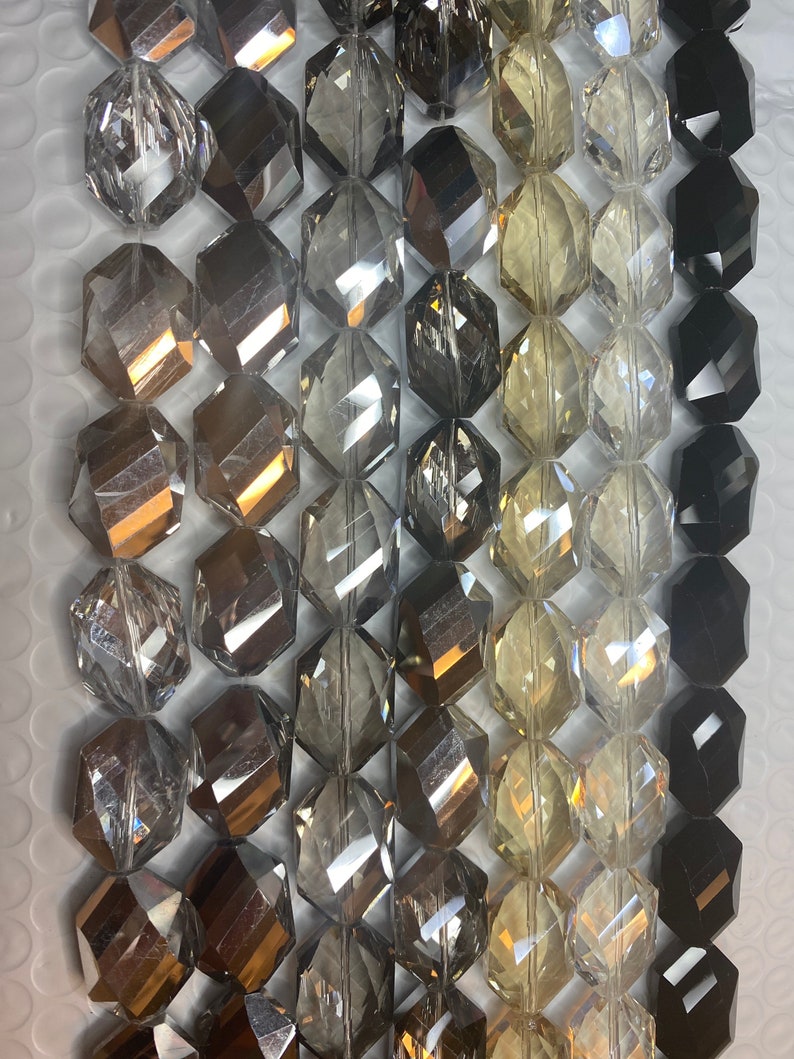 Peut inclure: Un brin de perles de verre facett&eacute;es dans diff&eacute;rentes nuances de gris, noir et transparent. Les perles sont hexagonales et ont une finition polie.