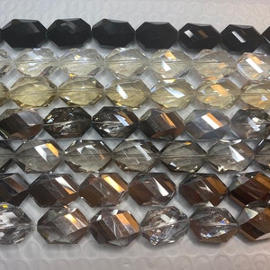 Peut inclure: Gros plan sur une vari&eacute;t&eacute; de perles en verre facett&eacute;es dans diff&eacute;rentes nuances de gris, noir et transparent. Les perles sont dispos&eacute;es en rang&eacute;es, les perles noires en haut et les perles transparentes en bas.