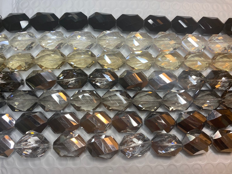 Peut inclure: Gros plan sur une vari&eacute;t&eacute; de perles en verre facett&eacute;es dans diff&eacute;rentes nuances de gris, noir et transparent. Les perles sont dispos&eacute;es en rang&eacute;es, les perles noires en haut et les perles transparentes en bas.