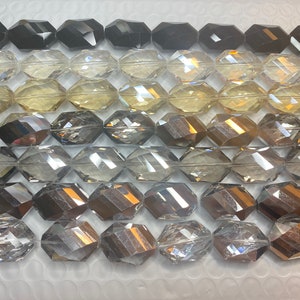 Peut inclure: Une collection de perles en verre facett&eacute;es dans diff&eacute;rentes nuances de gris, noir et transparent. Les perles sont de forme ovale et ont une finition brillante et r&eacute;fl&eacute;chissante.