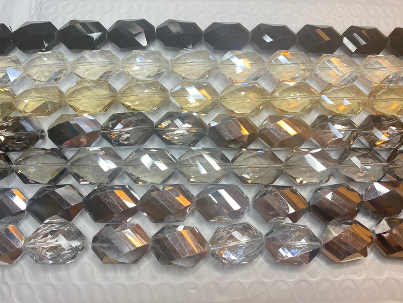 Peut inclure: Une collection de perles en verre facett&eacute;es dans diff&eacute;rentes nuances de gris, noir et transparent. Les perles sont de forme ovale et ont une finition brillante et r&eacute;fl&eacute;chissante.