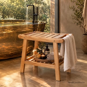 May include: A rectangular wooden shower bench with a slatted top and a lower shelf. A white textured towel hangs over the side. The lower shelf holds a wooden tray with a small brown bottle, a sponge, a candle, and folded towels. WoodCarvedStories.