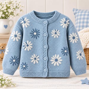 Peut inclure: Un gilet en tricot bleu clair orné d'un motif répétitif de fleurs blanches et bleu foncé ressemblant à des marguerites. Le vêtement présente une encolure ronde, des manches longues à bords-côtes et une fermeture à cinq boutons assortis.