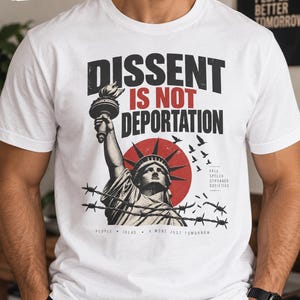 May include: A white t-shirt featuring a graphic of the Statue of Liberty behind barbed wire with a red sun background. The text reads DISSENT IS NOT DEPORTATION, FREE SPEECH STRONGER SOCIETIES, and PEOPLE IDEAS A MORE JUST TOMORROW in black and red.