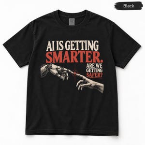 Könnte beinhalten: Ein schwarzes T-Shirt mit kurzen Ärmeln und einem Grafikdruck, der eine Roboterhand und eine menschliche Hand zeigt, die aufeinander zugehen. Der Text lautet AI IS GETTING SMARTER. ARE WE GETTING SAFER? mit einem kleinen roten Stern.