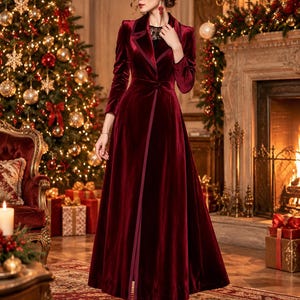 May include: A floor-length, deep burgundy velvet coat dress featuring long sleeves, a notched lapel collar, and a single button closure at the waist. The garment has a structured bodice and a full, flowing skirt with a vertical front seam.