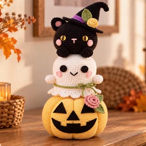Può includere: Una decorazione all'uncinetto impilata composta da una zucca gialla alla base, un fantasma bianco al centro e un gatto nero con un cappello da strega bordato di viola in cima. Le figure sono decorate con piccoli fiori realizzati all'uncinetto.