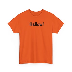 May include: A bright orange short-sleeved t-shirt featuring the word Hellow! printed in black across the centre of the chest. The text includes a small black dot below the letter w and a small black outline of a mouth next to the exclamation point.