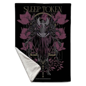 May include: A black rectangular throw blanket featuring the text SLEEP TOKEN at the top. The graphic displays a central dark figure with a horned head, surrounded by purple flowers, vines, and geometric lines. One corner is folded to show white fleece.