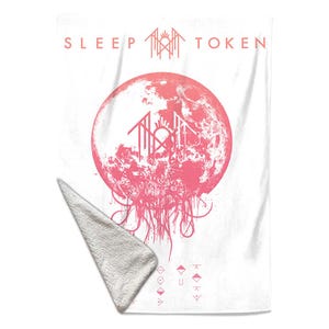 May include: A white rectangular throw blanket featuring a pink graphic of a moon with a central geometric symbol and the text SLEEP TOKEN. The design includes dripping lines at the bottom of the moon and a series of small symbols at the base.