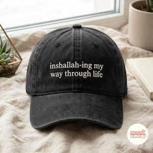 Peut inclure: Une casquette de baseball noire avec une visière courbée et une construction à six panneaux. L'avant de la casquette présente le texte blanc brodé "inshallah-ing my way through life" centré dans une police sans empattement.