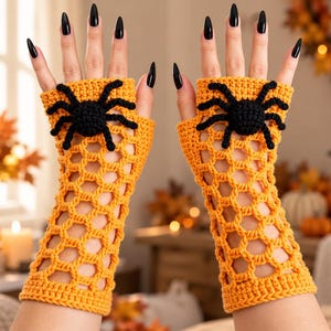 May include: A pair of orange fingerless gloves featuring a crocheted open-weave web pattern and a prominent black spider appliqué on the back of each hand. The gloves extend from the knuckles to the mid-forearm with a ribbed cuff.