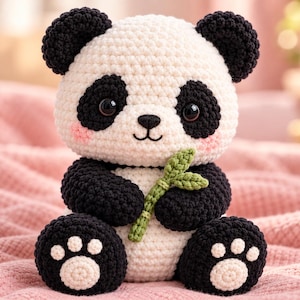 Puede incluir: Un juguete de panda tejido a ganchillo con cuerpo blanco y orejas, parches oculares, brazos y piernas negros. El panda tiene ojos grandes y oscuros, una nariz pequeña negra y mejillas rosadas. Sostiene un pequeño tallo de bambú verde tejido.