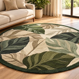 May include: A round area rug featuring a large-scale botanical pattern of overlapping leaves in various shades of forest green, sage, and cream. The rug has a thick, dark green border and a textured, tufted surface with defined leaf veins.