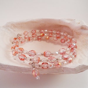 Op de afbeelding: Een meerstrengige armband gemaakt van roze en heldere glazen kralen. De armband is om een ​​witte schelp gewikkeld.