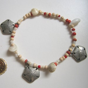 May include: Two bracelets with white and red beads. One bracelet has a gold bottle cap charm with the word "BEER" on it. The other bracelet has three silver starfish charms and white and orange beads.