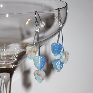 May include: A pair of dangle earrings with blue and white glass beads shaped like leaves. The earrings are hanging from a martini glass.