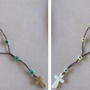 May include: Two necklaces with a cross pendant and colourful beads. One necklace has blue and green beads, the other has yellow beads.