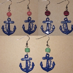 Könnte beinhalten: Ein Paar blaue Ankerohrringe mit gestreiften Perlen. Die Perlen sind rot-weiß, schwarz-weiß und grün-weiß.