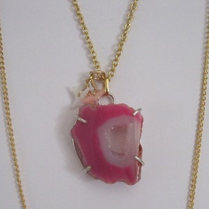 Peut inclure: Un collier en chaîne dorée avec un pendentif en agate rose et blanche. Le pendentif est attaché à la chaîne par un fermoir doré. La chaîne est également ornée de petits charms dorés et blancs.