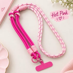 May include: A phone lanyard featuring a dual-tone design with solid hot pink cord and light pink cord patterned with small dark pink hearts. The lanyard includes a rectangular hot pink attachment tab and a circular metal ring for secure device connection.