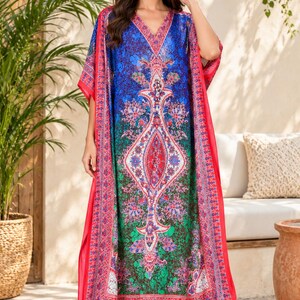 Puede incluir: Un vestido caftán largo hasta el suelo con un vibrante estampado inspirado en cachemira en tonos azul, verde y rojo. La prenda presenta un escote en V, mangas anchas y fluidas, y un borde rojo llamativo a lo largo de los extremos.