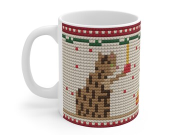 May include: A white ceramic mug featuring a printed pattern that mimics a knitted texture. The design displays a brown spotted cat reaching for a red ornament hanging from a green garland, set against a beige background with red accents.