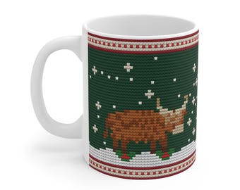 May include: A white ceramic mug featuring a dark green background with a cross-stitch pattern of a brown Highland cow standing in snow. The design includes white snowflakes and a red and white geometric border at the top and bottom edges.