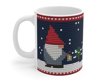 May include: A white ceramic mug featuring a dark blue knit-patterned graphic of a gnome wearing a red hat, holding a lantern in a snowy landscape with a small green tree. The design includes red and white decorative borders at the top and bottom.