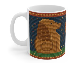 May include: A white ceramic mug featuring a printed design of a brown dog sitting on green grass against a dark blue background. The pattern mimics a knitted texture with a decorative border of red and yellow squares at the top and bottom.