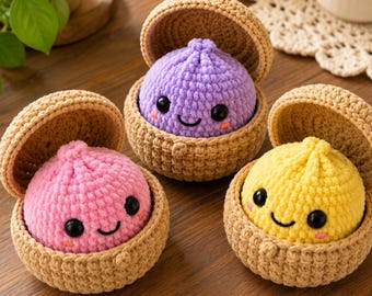May include: Three crocheted plush toys, each featuring a round, colorful character nestled inside a tan, lidded basket. The characters are pink, purple, and yellow, all with black safety eyes, stitched smiles, and small pink cheeks.