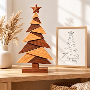 May include: A decorative wooden Christmas tree sculpture composed of alternating light and dark brown triangular wood segments, topped with a wooden star and mounted on a rectangular base, standing next to a framed line drawing of a tree.