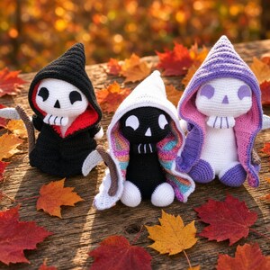 Puede incluir: Tres figuras de ganchillo con rostros en forma de calavera y capuchas puntiagudas. La figura de la izquierda es negra con interior rojo, la central es negra con capucha blanca y forro arcoíris, y la de la derecha es blanca con capucha y forro morados.