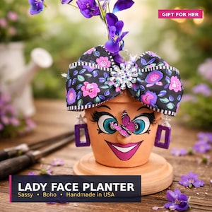 May include: A terracotta planter shaped like a face with painted blue eyes, long eyelashes, and a pink mouth. It features a black floral bow with a rhinestone center, purple rectangular earrings, and a small purple butterfly on the nose.
