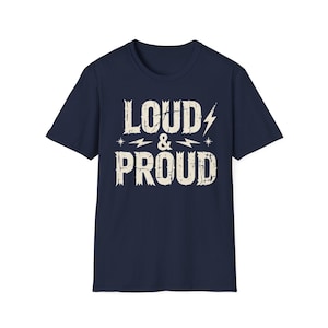 May include: A navy blue short-sleeve t-shirt featuring the text LOUD & PROUD in a distressed, off-white, block-style font. The design includes two small lightning bolt icons and two star icons flanking the ampersand on the front of the shirt.
