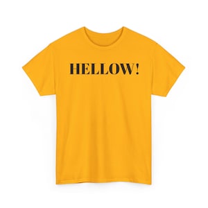 May include: A bright golden yellow short-sleeved t-shirt featuring the word HELLOW! printed in a bold, black, serif font across the centre of the chest. The garment has a standard crew neckline and a straight hemline at the bottom.