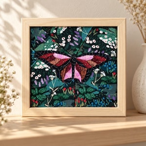 May include: A square framed fabric art piece featuring a central butterfly with pink, red, and brown wings. The background is a dark green fabric printed with a botanical pattern of small white, red, and purple flowers and green foliage.