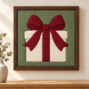 May include: A square wall art piece featuring a cream-coloured gift box with a large, deep red bow and ribbon, set against a textured olive green background, all enclosed within a dark brown wooden frame.