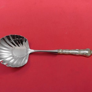 May include: A silver serving spoon with a scalloped bowl and an ornate handle. The spoon is on a red background.